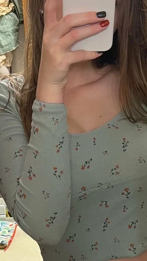 Woman in floral long-sleeve top taking mirror selfie, hair covering face
