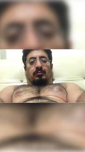man with glasses and beard lying shirtless in a bedroom setting