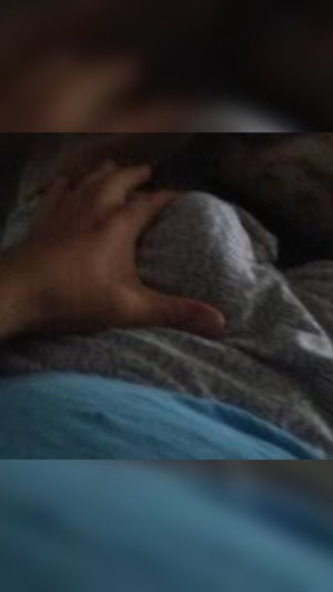 Hand resting on patterned fabric, possibly a bedsheet, in dim lighting.