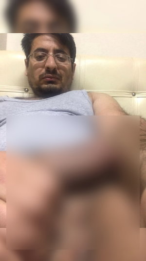 Man with glasses and beard wearing gray tank top lying on bed.