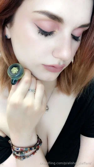 Woman with short red hair, wearing black top, holding small object, indoor setting.