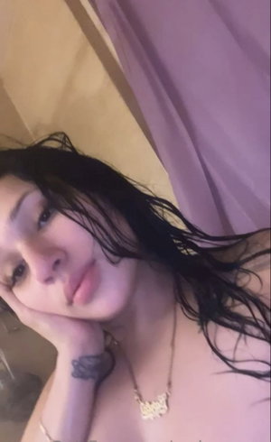Topless woman with wet black hair, necklace, in bathroom.