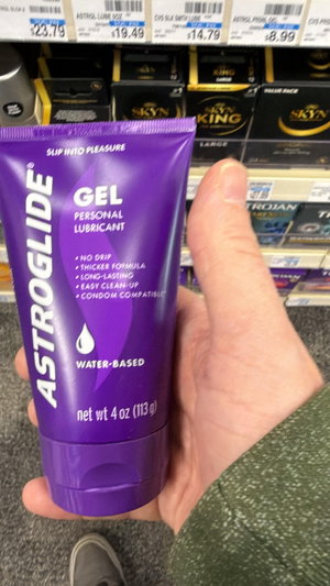 Hand holding purple lubricant tube in store aisle.
