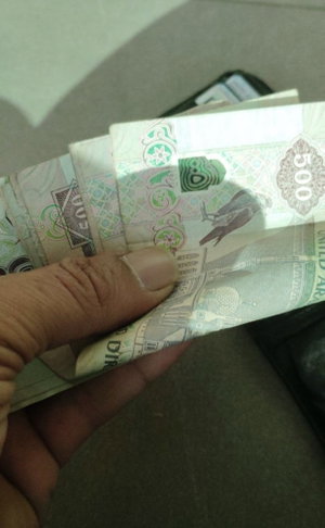 Hand holding a stack of 500 denomination banknotes indoors.
