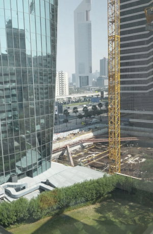 Cityscape with tall glass buildings, construction crane, and greenery below.