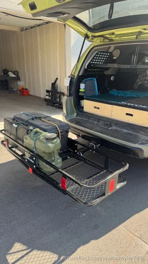 Open SUV trunk with storage system and cargo rack holding jugs, in a garage setting.