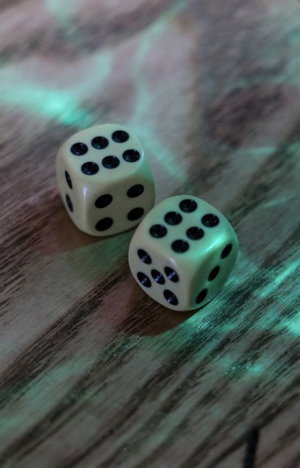 Two white dice with black dots on a wooden surface under green lighting.