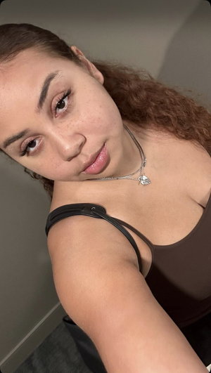 Curly-haired woman in brown strap top, indoor selfie.