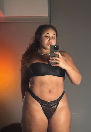 Woman in black strapless top and lace thong taking mirror selfie indoors.