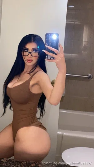 Woman with long black hair in brown bodysuit taking mirror selfie in bathroom.
