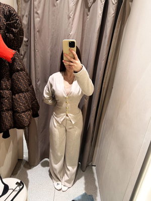 Woman in beige cardigan and pants takes mirror selfie in fitting room.