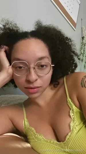 Woman with curly hair and glasses in a green lace top, indoors.