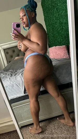Woman with blue braids in light blue thong taking mirror selfie in bedroom.