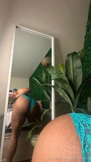 Woman in teal lace underwear taking mirror selfie in bedroom with green wall and plant.