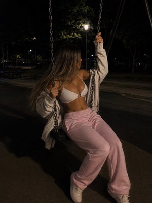 Woman in white bra and pink pants on swing at night.