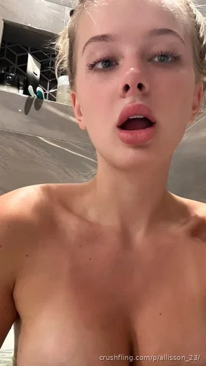 Woman with blonde hair, bare shoulders, topless, in a bathroom setting.