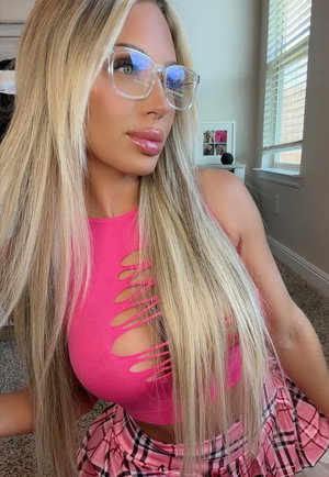 Woman with long blonde hair wearing pink cutout top and plaid skirt indoors.