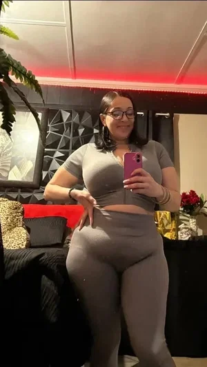 Woman in gray crop top and leggings takes mirror selfie in bedroom.