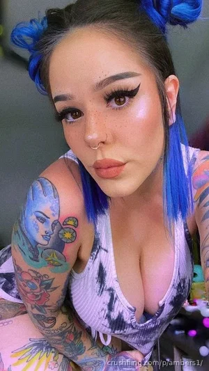 Woman with blue hair and tattoos wearing a tie-dye top, indoors.