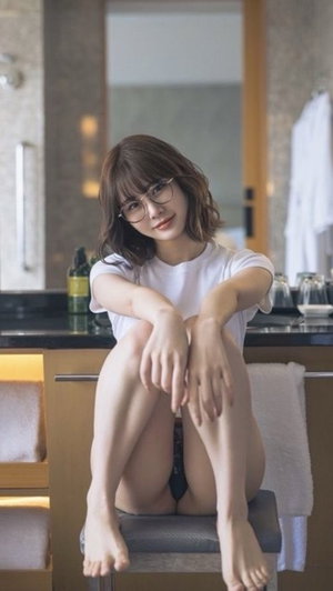 Asian woman with glasses in white t-shirt sitting in bathroom.