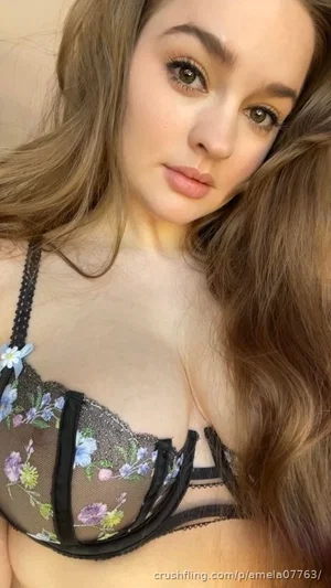Woman with long brown hair wearing floral lace bra, close-up selfie indoors.