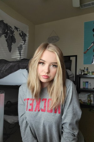 Blonde woman in gray sweatshirt in bedroom.