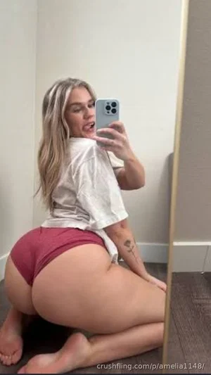 Woman with blonde hair in white shirt and red underwear posing in mirror selfie indoors.