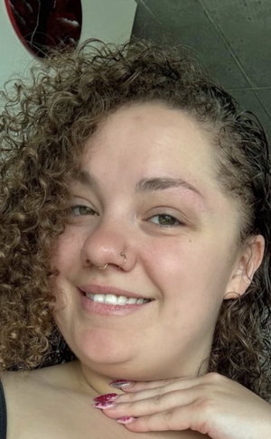 Woman with curly hair and nose ring smiling indoors.