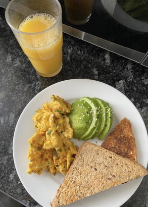 Breakfast plate with eggs, avocado, toast and juice on counter.