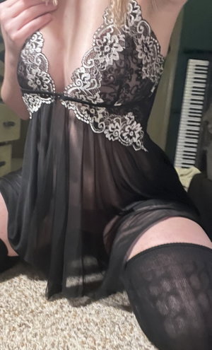 Woman in black lace lingerie and stockings sitting indoors.