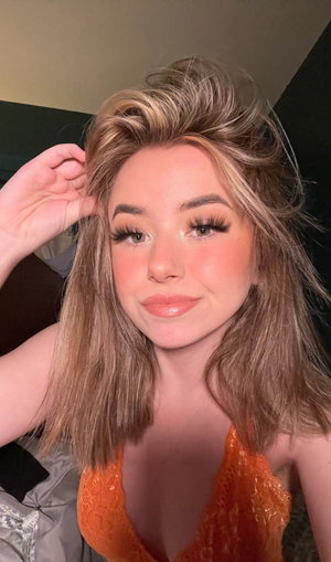 Blonde woman in orange lace top taking indoor selfie.