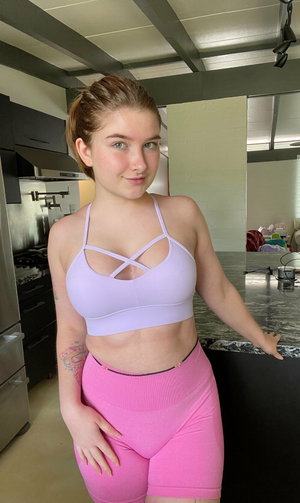 Woman in purple sports bra and pink shorts in kitchen.