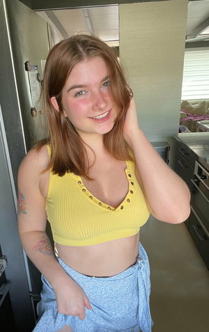 Woman with light brown hair in yellow top and blue skirt indoors.