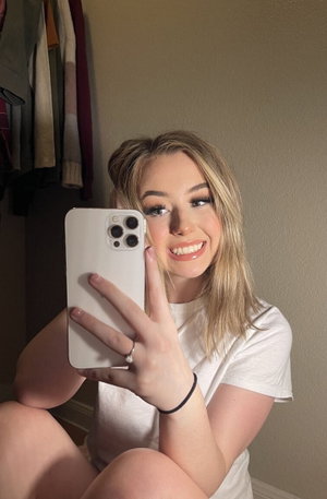 Blonde woman in white t-shirt taking selfie indoors.