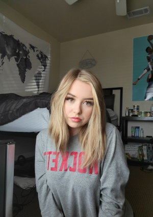Blonde woman in grey sweatshirt in bedroom.