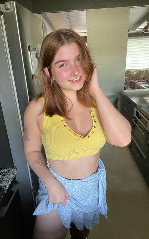 Woman with brown hair in yellow top and blue skirt in kitchen.