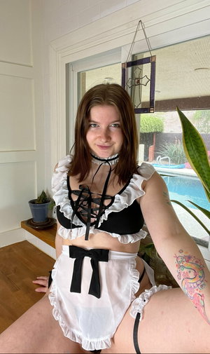 Woman in maid outfit taking indoor selfie by window.