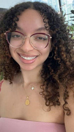 Curly haired woman in glasses and pink top indoors.