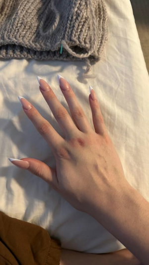 Hand with manicured nails on white sheets near gray knitwear.