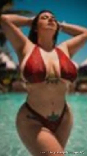 Woman in red bikini standing in pool, hands in hair, outdoor setting.