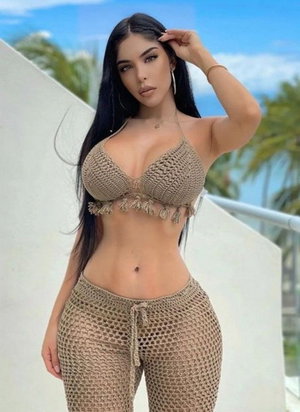 Woman in beige crocheted top and pants posing outdoors with palm trees.