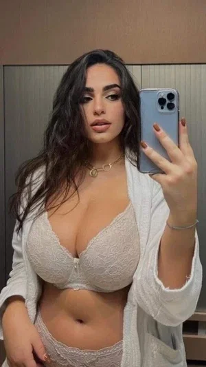 Woman in white lace lingerie and robe takes mirror selfie indoors.