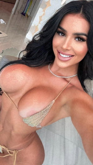 Woman with long dark hair in a beaded bikini top, posing indoors.