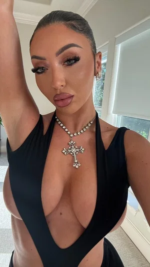 Woman in black plunging top with cross necklace, indoors, posing for selfie.