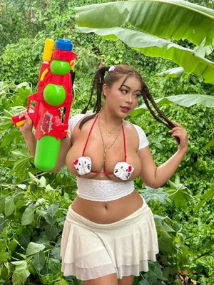 Woman in white Hello Kitty bikini top and skirt holding water gun in lush green garden.