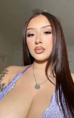 Woman with long dark hair in purple lace top taking selfie indoors.