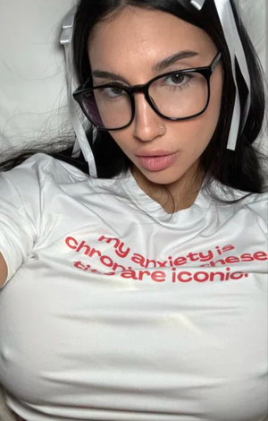 Woman with dark hair and glasses in white t-shirt indoors.