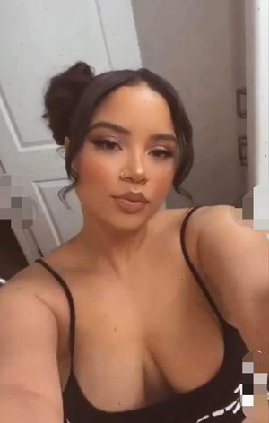 Woman with dark hair in bun wearing black top taking selfie indoors.