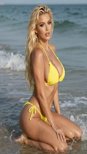 Blonde woman in yellow bikini kneeling in ocean waves at beach.