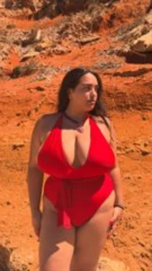 Woman in red swimsuit standing on rocky terrain outdoors.